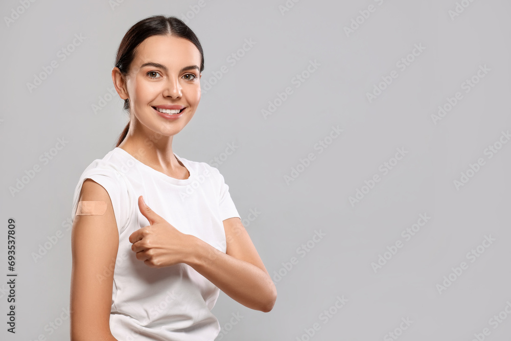 Woman with sticking plaster on arm after vaccination showing thumbs up against light grey background, space for text Woman with sticking plaster on arm after vaccination showing thumbs up against light grey background, space for text