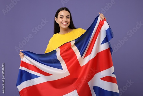 Happy young woman with flag of United Kingdom on violet background