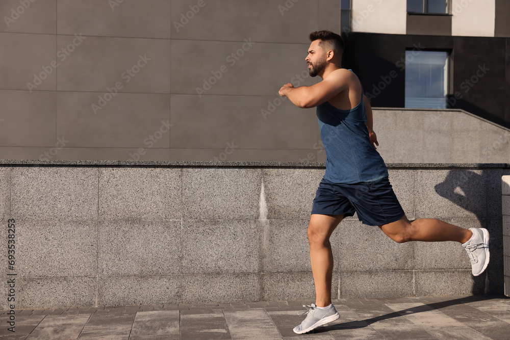 Naklejka premium Young man running near building outdoors. Space for text