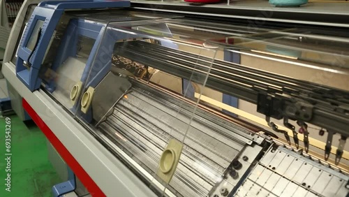 View of working knitting machine in workshop. A row of industrial textil flat knitting machines in a knitwear factory. Manufacture of knitwear, modern computerized flat Knitting Machine