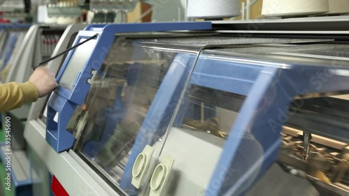 The operator sets up a modern digital knitting machine. A row of industrial textil flat knitting machines in a knitwear factory. Manufacture of knitwear, modern computerized flat Knitting Machine