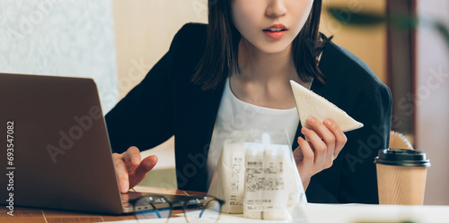 サンドイッチを食べながら仕事をする忙しい日本人ビジネスウーマン photo