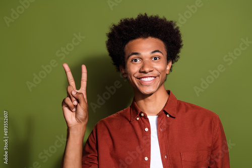 Portrait of good mood optimistic guy with chevelure hairdo wear stylish shirt showing v-sign symbol isolated on green color background