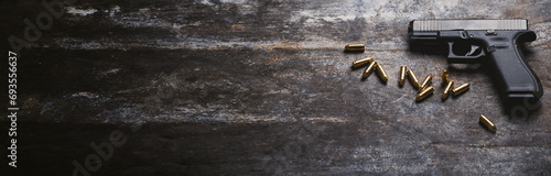 Hand gun with ammunition on dark background. 9 mm pistol military weapon and pile of bullets ammo at the metal table. Banner or wide panorama. photo