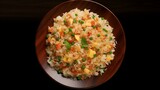 Fried rice with meat and vegetables on a wooden plate on a black background