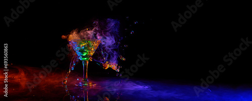 Glass of martini cocktail standing against dark background with neon light with smoke. Splashes. Concept of alcohol drink, nightclub, party, taste, celebration. Banner. Empty space to insert text