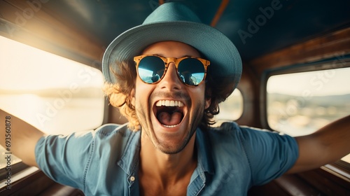 Cheerful man capturing a travel selfie with stylish hat and trendy sunglasses, blurred background