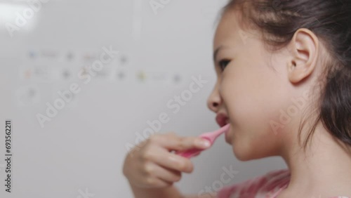 Close up and side view of face and mouth of Adorable Asian girl is in happiness for her brushing her teeth routinely in the morning in clean and bright bathroom for healthy dental care of kid. photo
