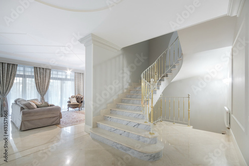A hall with a marble staircase and gilded railings in a luxurious mansion. Living room .with panoramic windows and classic furniture. photo