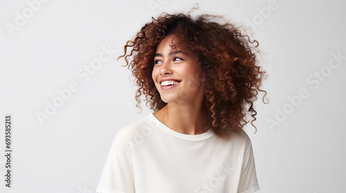 A woman with curly hair is laughing joyfully, keeping her hands on her chest, and concentrating above her head while being isolated on a white background with blank copy space. she is photo