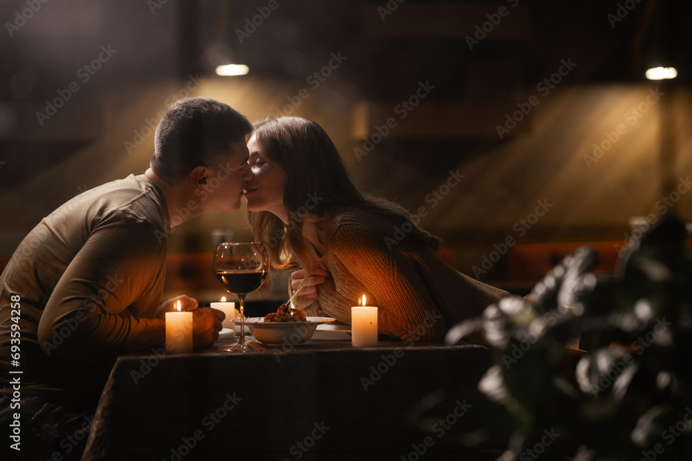 Couple in love celebrating Valentine's day having dinner at home, kissing, view through the window - obrazy, fototapety, plakaty 