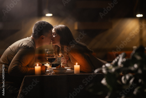 Couple in love celebrating Valentine's day having dinner at home, kissing, view through the window photo