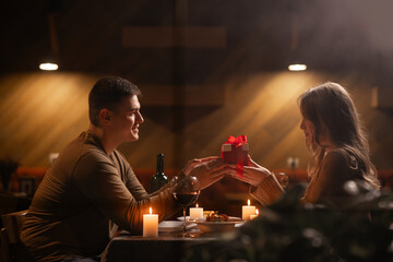Happy young couple celebrating Valentines day having romantic dinner at home. Loving man giving gift box his woman