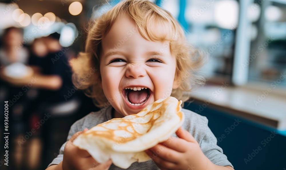 Cute baby with blond hair with a crepe on Mardi Gras, holding a mouth-watering pancake, laughing with delight, little greedy boy or girl with open mouth, smiling, thrilled and eager to taste the snack - obrazy, fototapety, plakaty 