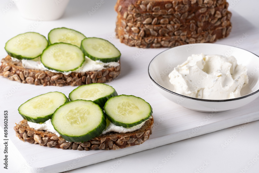 Rye bread with cream cheese and cucumbers on a white table. Whole grain rye bread with seeds Rye bread with cream cheese and cucumbers on a white table. Whole grain rye bread with seeds