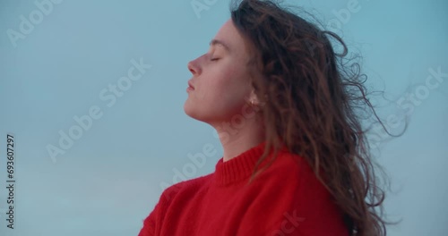 Cinematic portrait of young pensive woman breathe in fresh ocean breeze air, wind blow her hair around. Holistic and self love lifestyle. At peace with oneself. Self search and inner world photo