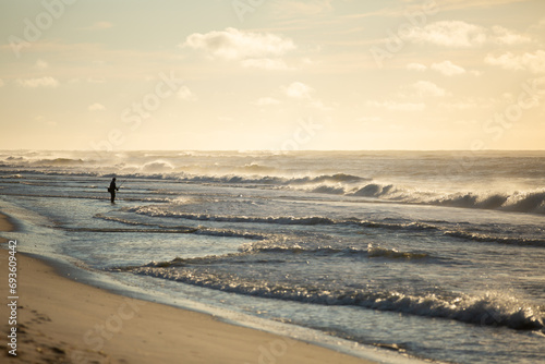 Fisherman silhouette on the beach surfcasting during a colorful sunrise. Robert Moses State Park, Long Island, New York.