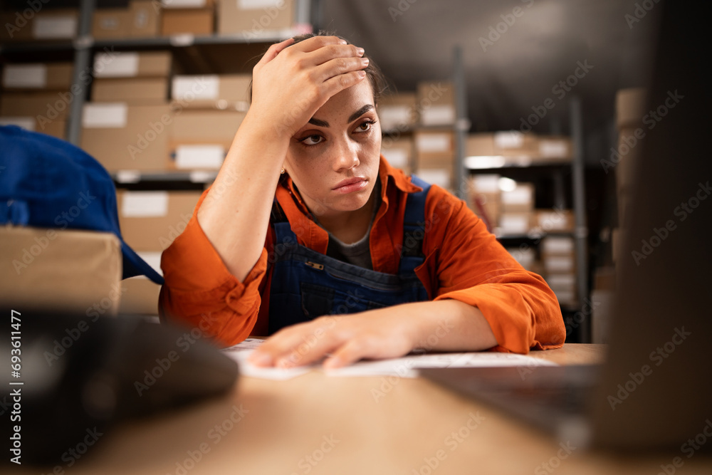 Warehouse worker on laptop while sitting at his working place. Tired woman working too long at computer. Exhausted worker Warehouse worker on laptop while sitting at his working place. Tired woman working too long at computer. Exhausted worker