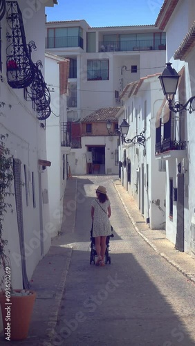 Mother strolling with newborn in a narrow street with white houses in picturesque village of Altea, Alicante, Spain photo