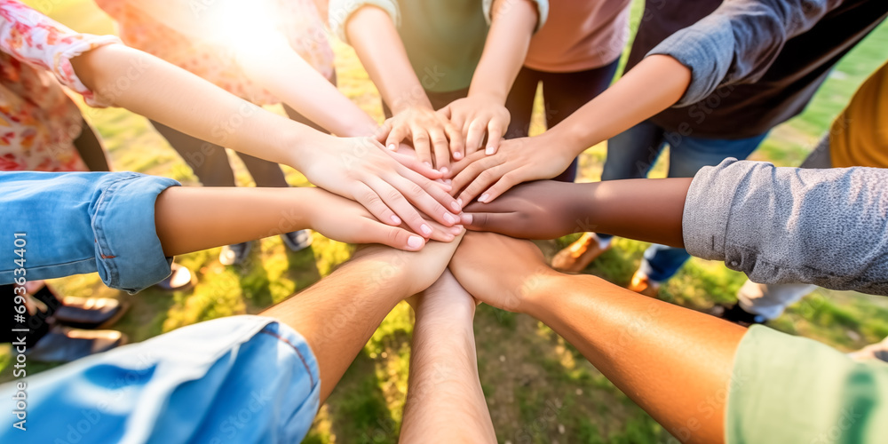 Fototapeta premium Multiethnic group of young people putting their hands on top of each other. Image of young students doing a stack of hands outdoors on a sunny day.