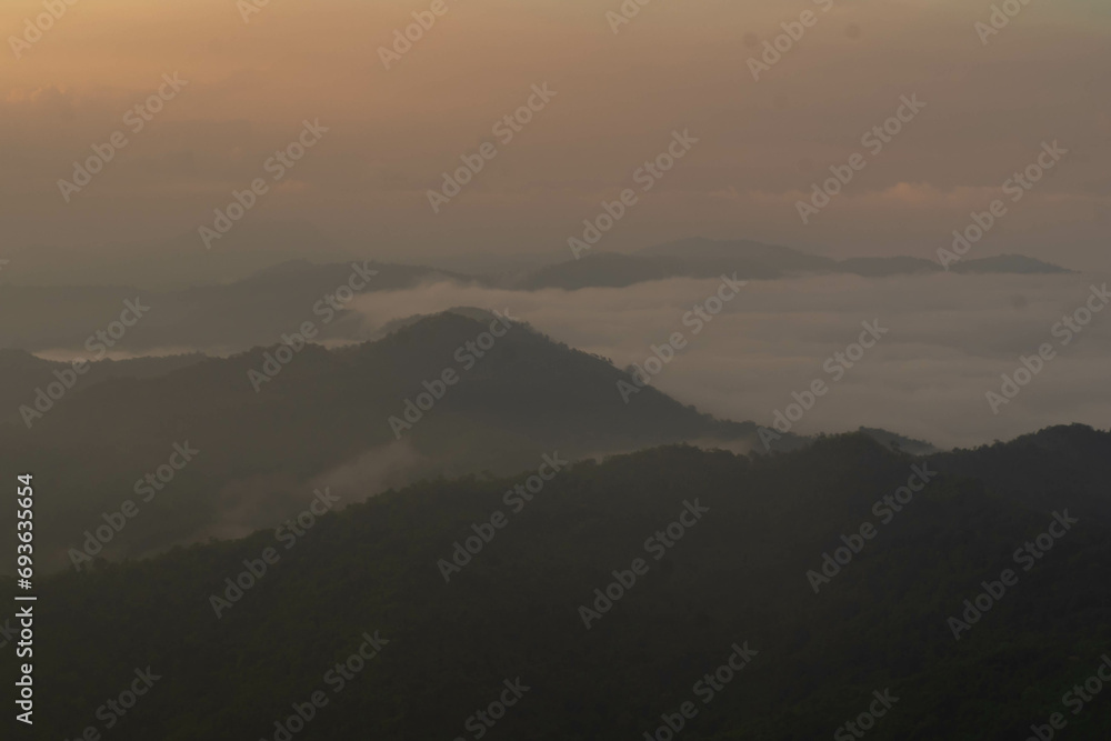 The stunning view from a tourist's standpoint as they go down a hill on a foggy trail with a hill and a background of a golden sky in Forest Park, Thailand. Bird's eye view. Aerial view.	