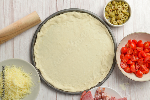 Various pizza components surrounding the pizza dough foundation