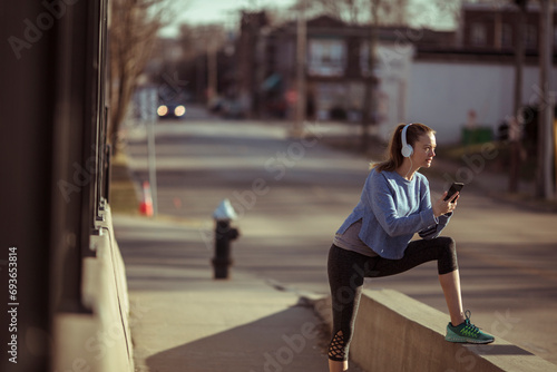 Fit young woman with headphones holding smartphone in street