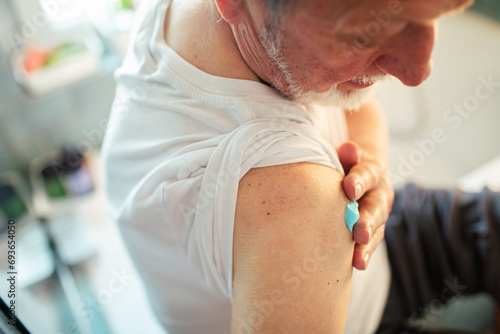 Close up senior man putting ointment on shoulder in bathroom photo