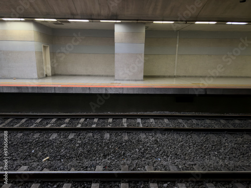 An empty, well-lit subway station platform with clean, patterned walls and two sets of tracks. The scene is desolate and quiet. railway with gravel. lonely sad concept.