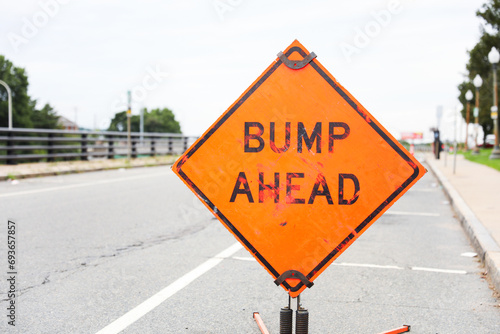 High-angle view of yellow speed bump on asphalt road, cautionary traffic sign nearby