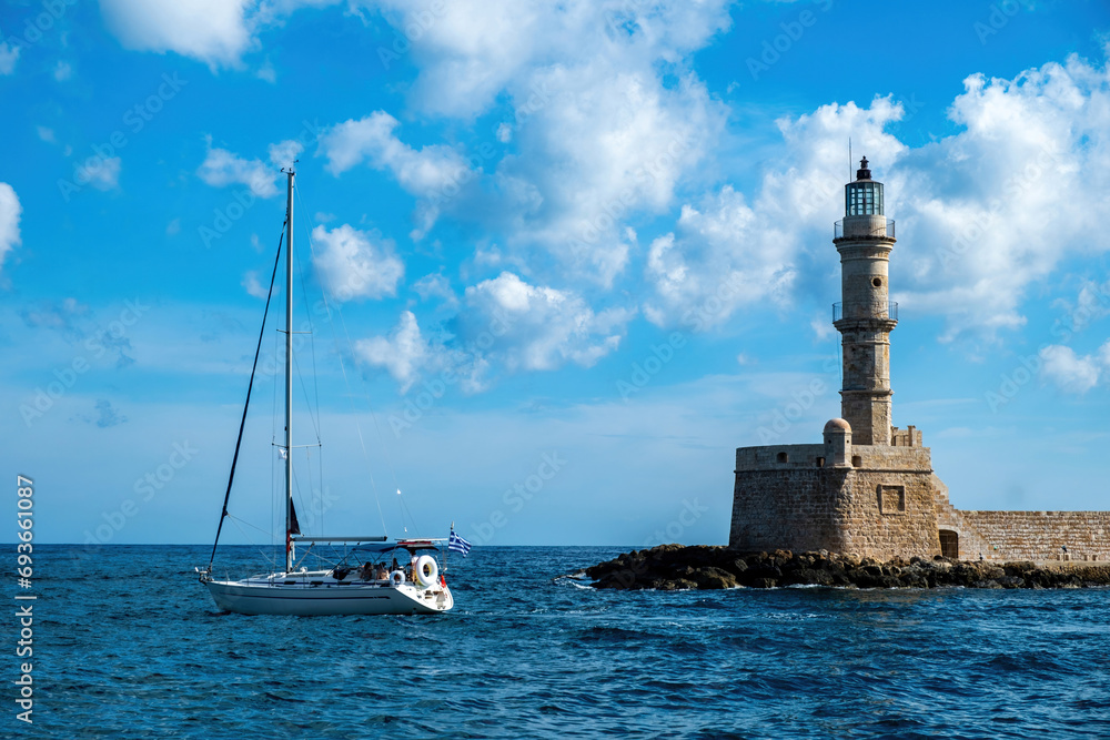 Lighthouse at Venetian harbour in Old Town of Chania Crete Greece. Boat sailing in ripple sea water.