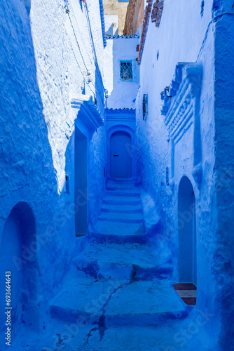 Narrow street with steps and some houses with old doors, all painted blue in the medina of Chefchaouen, Morocco