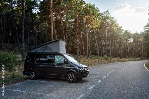Fototapeta Naklejka Na Ścianę i Meble -  Modern new camper van with the roof open parked beside the forest in beautiful nature scene at sunset, Well Rope Reservoir, Soria, Spain