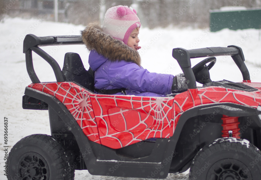 girl drives an electric toy car in winter on the street. Street toys. Children in a car with a battery.