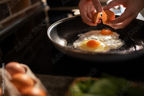 Hands cracking shell in pan making fried eggs in kitchen photo