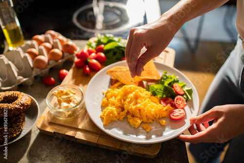 Woman hand adding salt to plate of scrambled eggs with salad photo