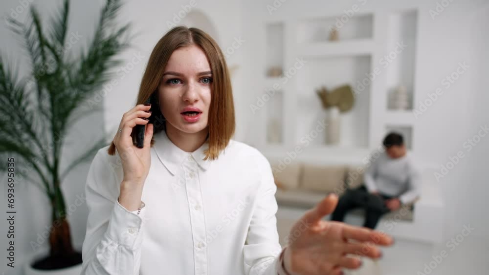 Brunette speaking on the phone, looking and pointing at camera. Lady opens mouth and covers it with hand in surprise. Man sits at backdrop in blur. Brunette speaking on the phone, looking and pointing at camera. Lady opens mouth and covers it with hand in surprise. Man sits at backdrop in blur.