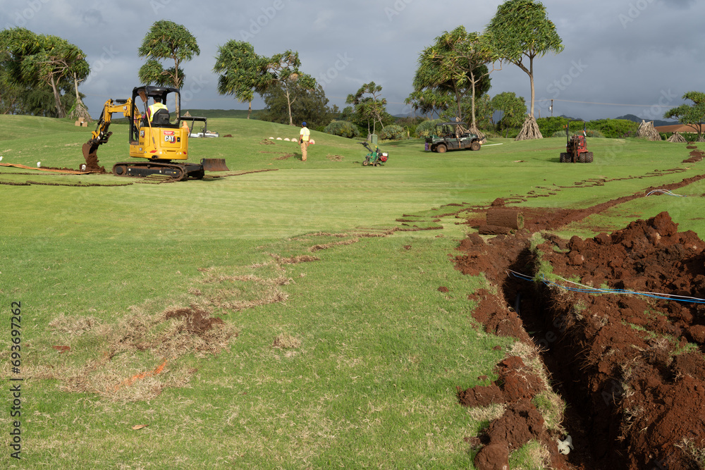 Man and construction equipment digging trenches through green grass of