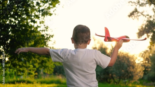 Happy child holds toy airplane on vacation in countryside. Small boy runs with airplane model. Healthy child plays with toy airplane dreaming to be pilot on vacation in meadow at free summer time #693705204