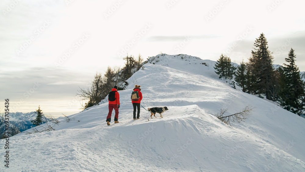 Couple enjoys a day outdoors climbing a snowy mountain with their dog in winter