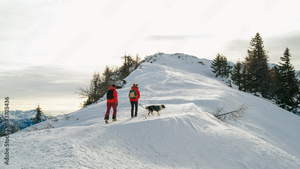 Couple enjoys a day outdoors climbing a snowy mountain with their dog in winter Couple enjoys a day outdoors climbing a snowy mountain with their dog in winter