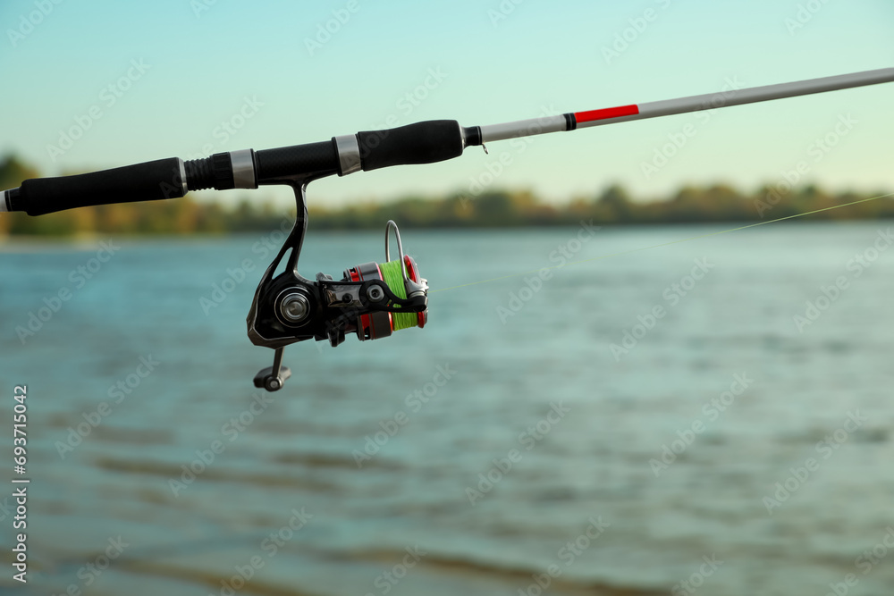 Fishing rod with reel near river, space for text Fishing rod with reel near river, space for text