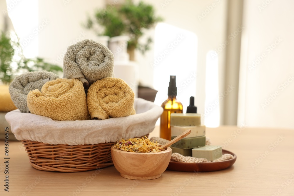 Dry flowers, soap bars, bottles of essential oils, jar with cream and towels on wooden table indoors, space for text. Spa time
