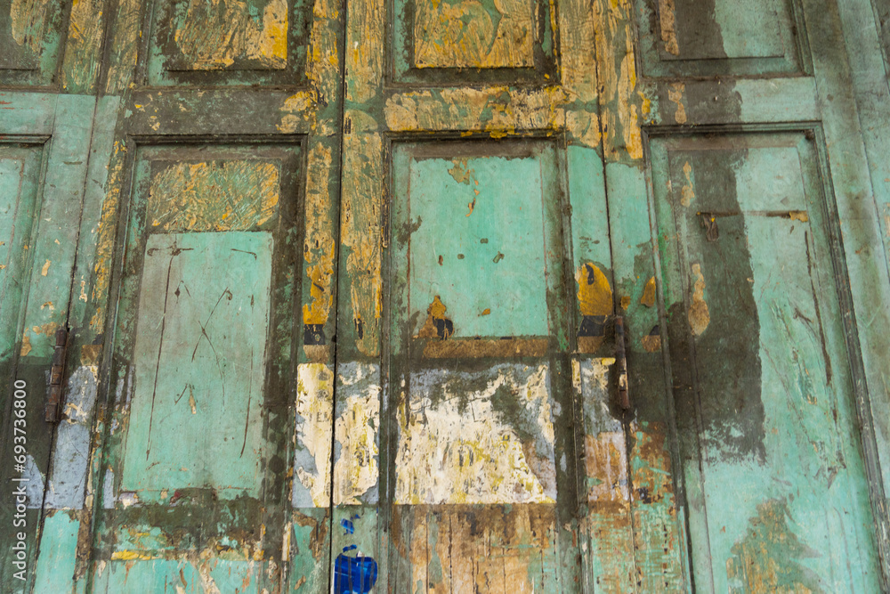 The background of the old door wall is made of wood, painted green, with clumps. Abstract wall texture backdrop. The background of the old door wall is made of wood, painted green, with clumps. Abstract wall texture backdrop.