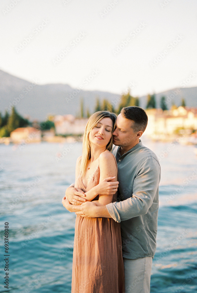 Man hugs woman from behind while standing on the seashore