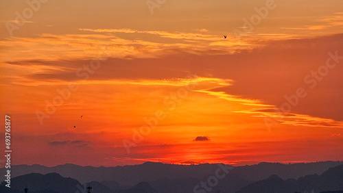 Beautiful sunset in the mountains. Sunset with beautiful orange evening sky and silhouette of mountains. Dramatic sunrise. Orange Sky. Bird in sky