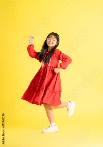 full body image of asian kid girl wearing dress and posing on yellow background 