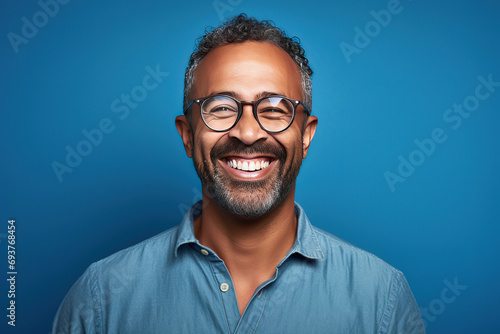 man with glasses on a blue background smiling at the camera