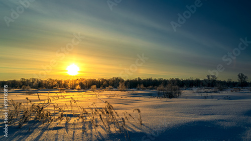 Winter sunrise in the field. Dry grass in the snow.