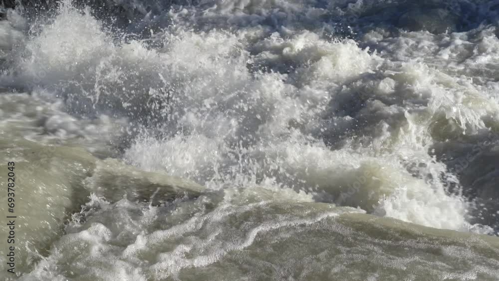 Close-up to the river swollen after heavy rainfall and flood water crashing through valley. The water flows fast from the high valley to the plain. General contest of a river in flood Close-up to the river swollen after heavy rainfall and flood water crashing through valley. The water flows fast from the high valley to the plain. General contest of a river in flood